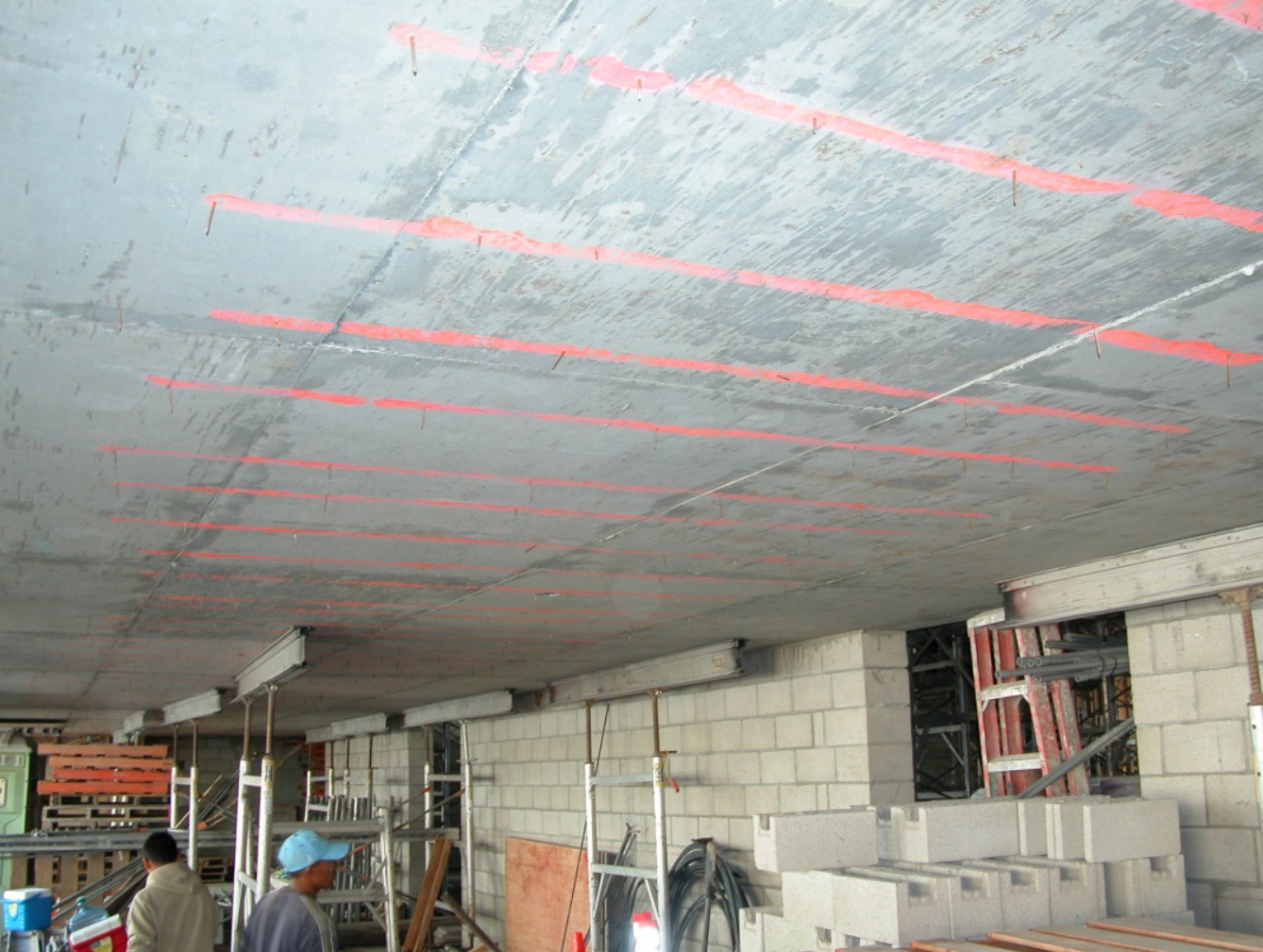 The concrete underside of a post tension slab marked with parallel red lines indicating the precise location of internal tendons to ensure safety during overhead drilling or anchoring.